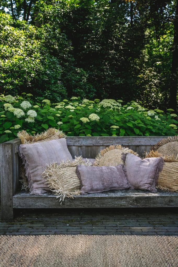 Houten bank met effen en franje kussens voor een boho vibe, omringd door groen in de tuin.