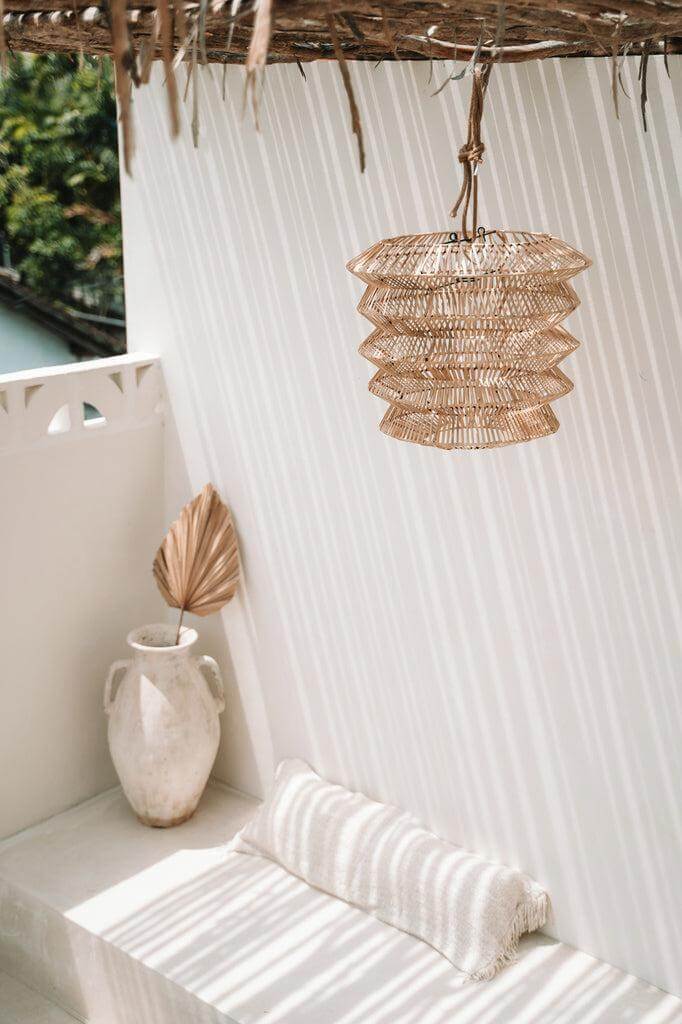 Charmante boho zithoek met crème kussenhoes en stijlvolle hanglamp in een zonnige patio.