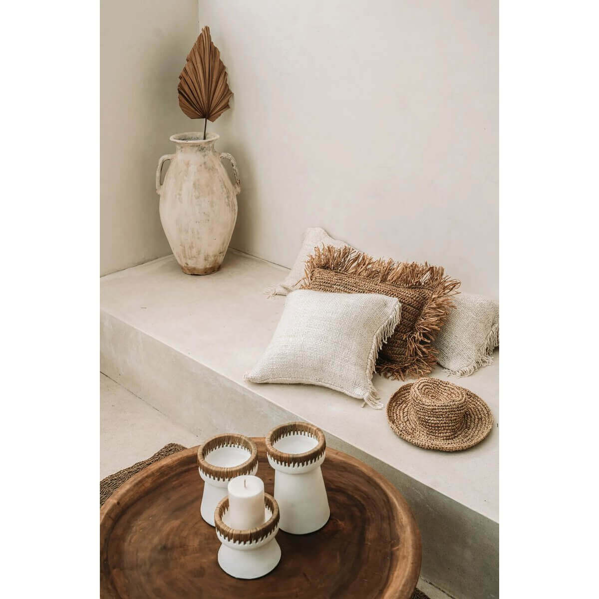 Boho interieur met crème kussenhoes, houten tafel en decoratieve kaarsen. Perfect voor woonkamer of terras.