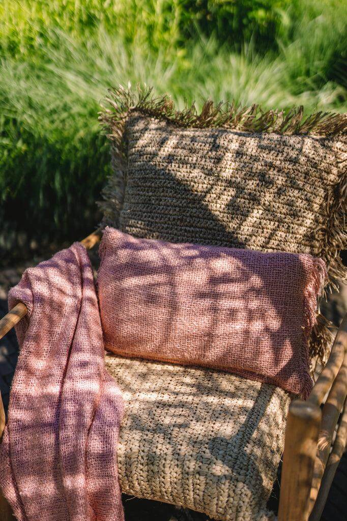Zalmroze kussenhoes op een boho-stoel in de tuin, voegt stijl en textuur toe aan interieur of terras, gemaakt van zacht katoen zonder binnenkussen.