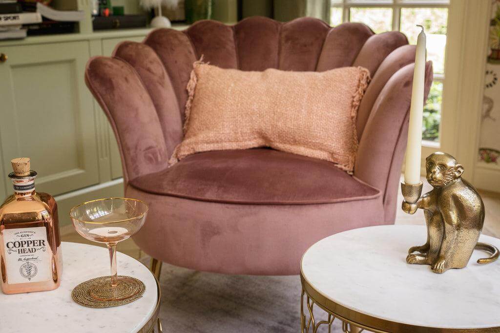 Gezellige zithoek met een zalm roze kussenhoes en fluwelen fauteuil, perfect voor een boho-stijl interieur met een chique accent.