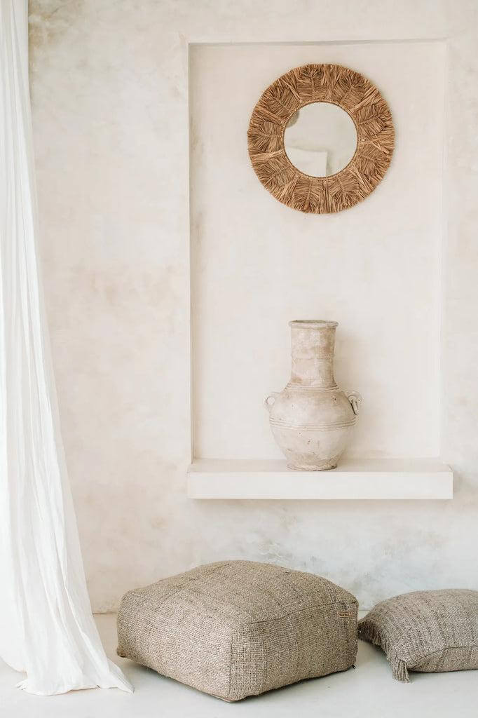 Stijlvolle beige katoenen poef perfect voor binnenruimtes, naast rustieke vaas en bohemian spiegel. Ontspanning in elegantie.