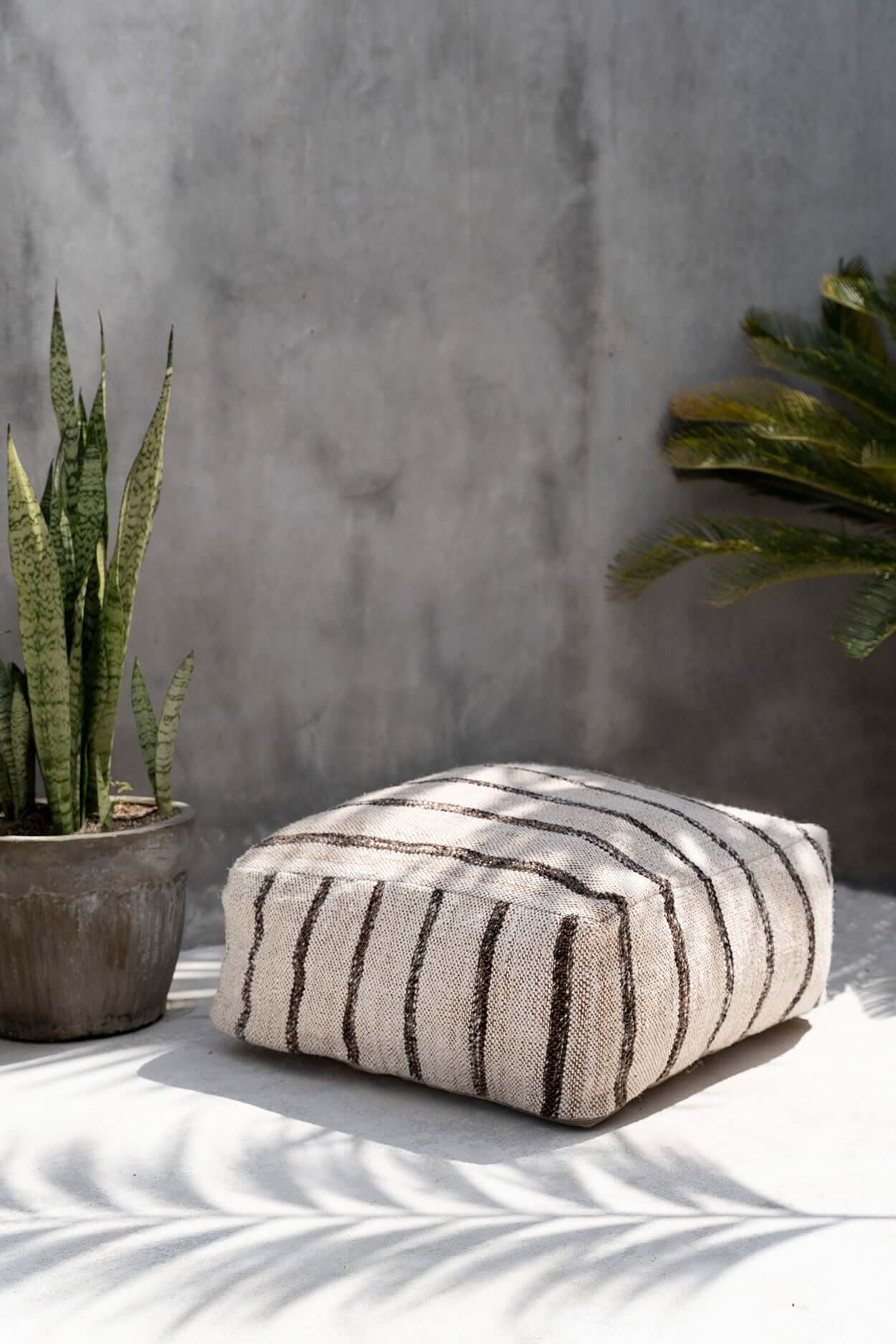 Bohemian witte katoenen poef met strepen, perfect voor stijlvol binnen- of buitengebruik, naast groene planten.