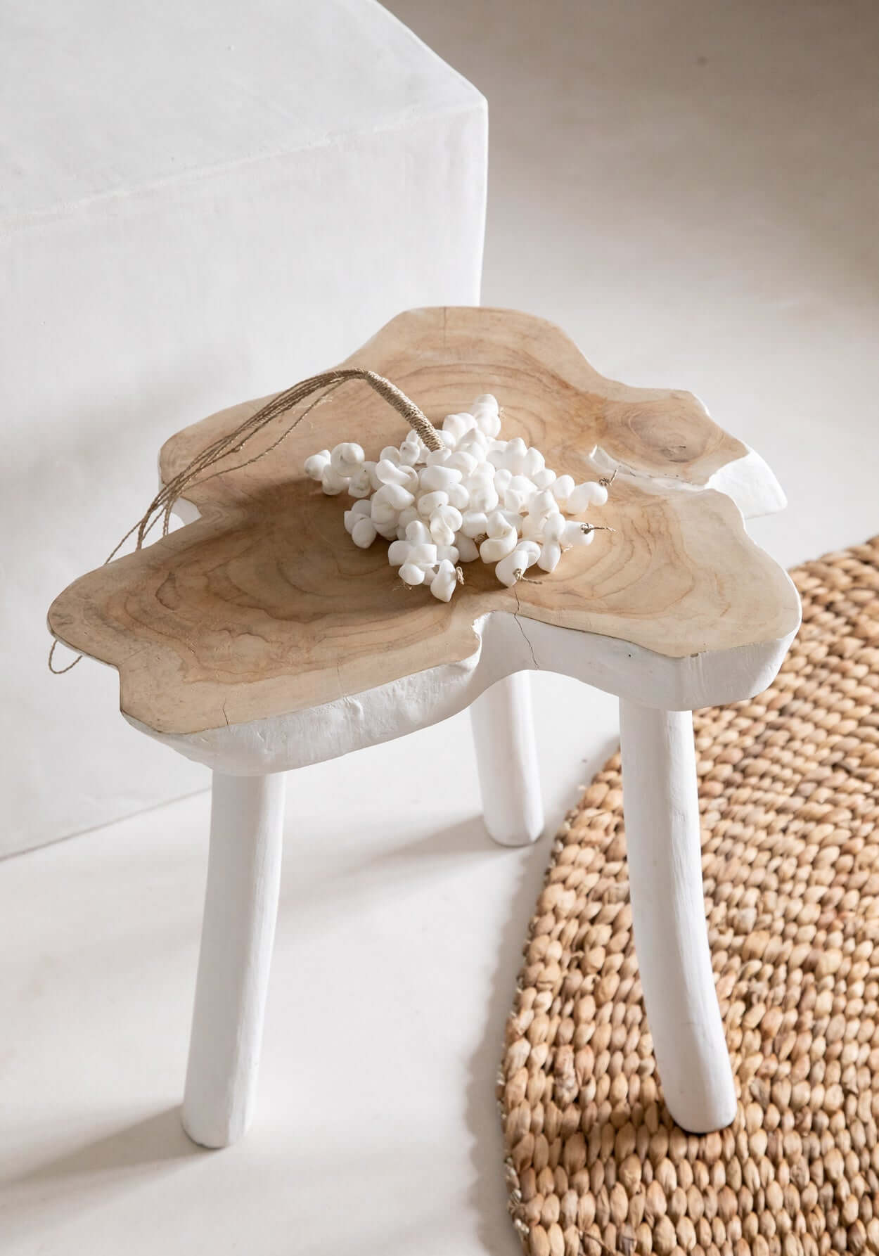 Organisch vormgegeven houten bijzettafel met natuurlijke witte afwerking en decoratieve bloem op een beige geweven kleed.