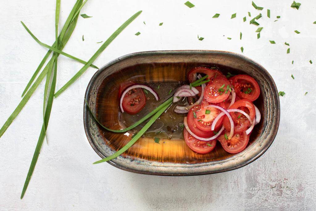 Ovale keramische kom met salade, kraakgeglazuurd servies uit de Comporta Collectie, versierd met tomaten en uien.