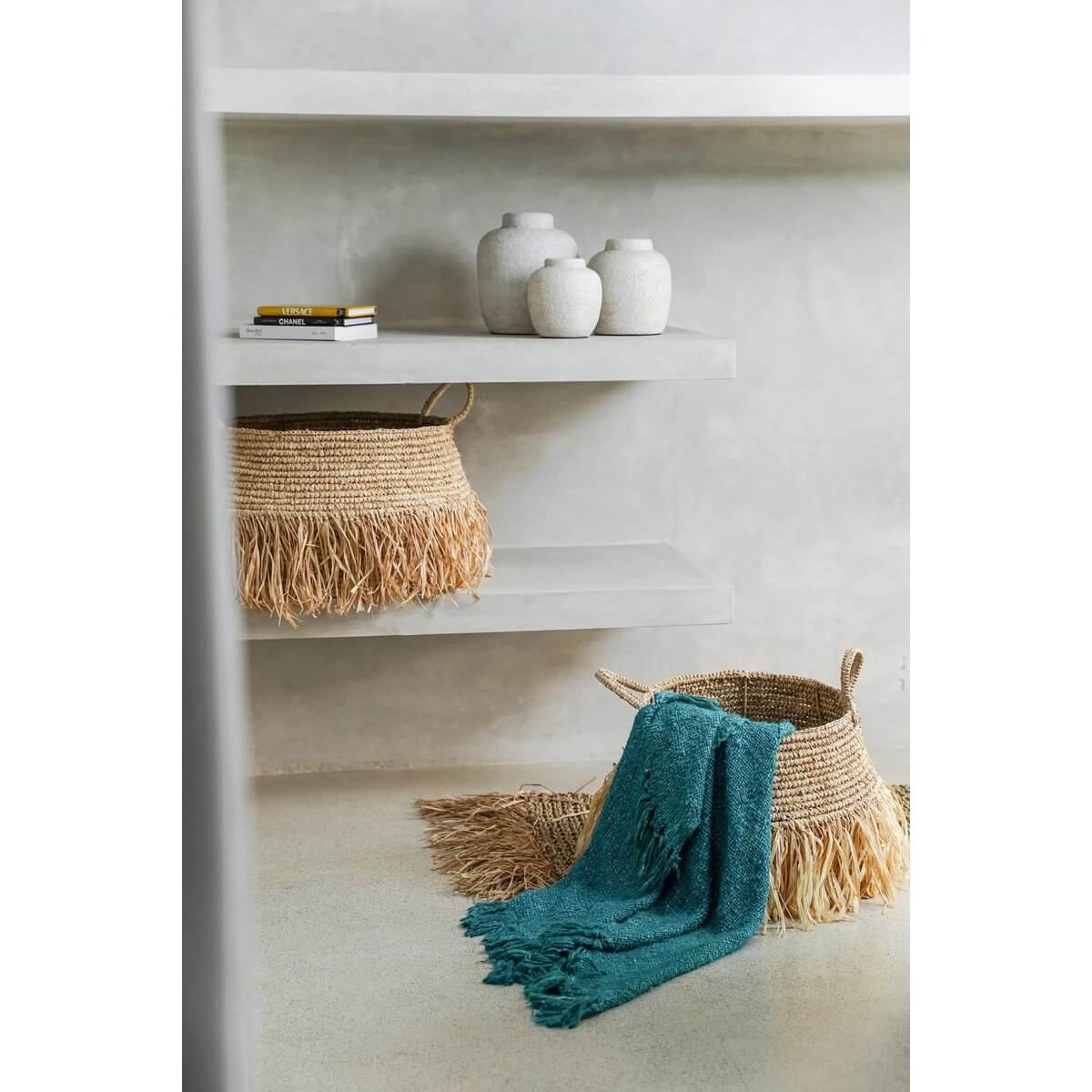 Bohemian style decor with wicker baskets, teal throw, and white vases on shelves in a cozy room.