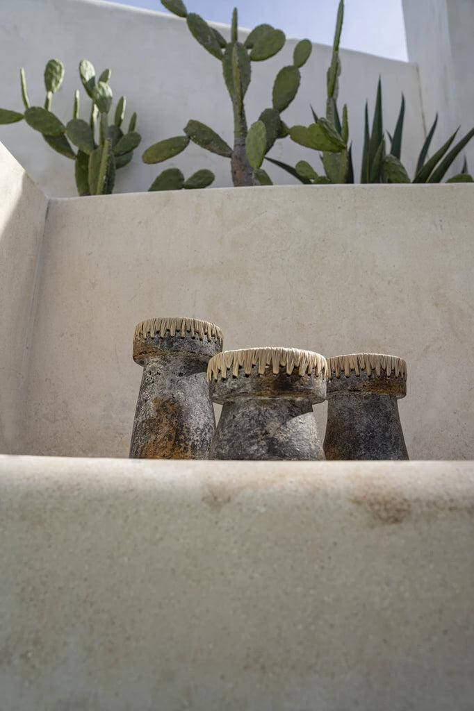 Drie antiek grijze De Pretty kaarsenhouders van terracotta met raffia-accenten op een trap voor cactussen.
