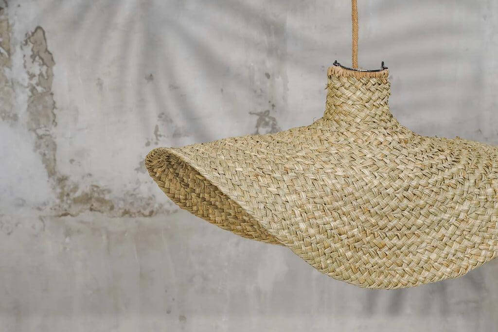 Natuurlijke geweven waterhyacint hanglamp "De Qubba" in organische vorm tegen een rustieke achtergrond.
