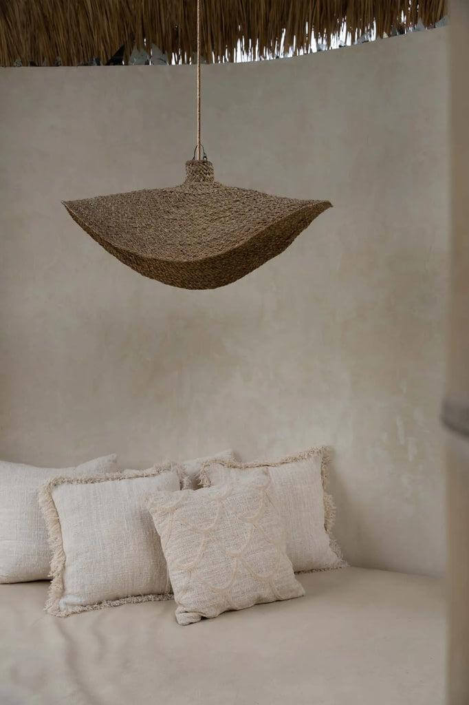 Natuurlijke Qubba hanglamp van waterhyacint boven een gezellige zithoek met kussens, geeft een rustieke en warme sfeer.