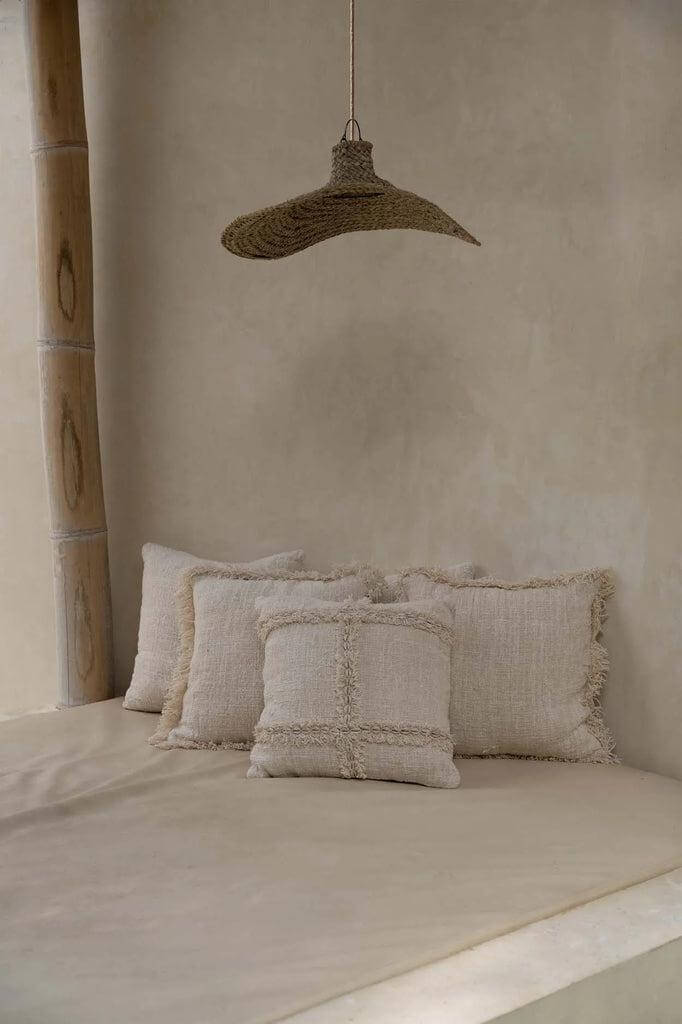 Alt Tag: "De Qubba hanglamp van geweven waterhyacint boven rustieke beige kussens, creëert een natuurlijke en sfeervolle ambiance."