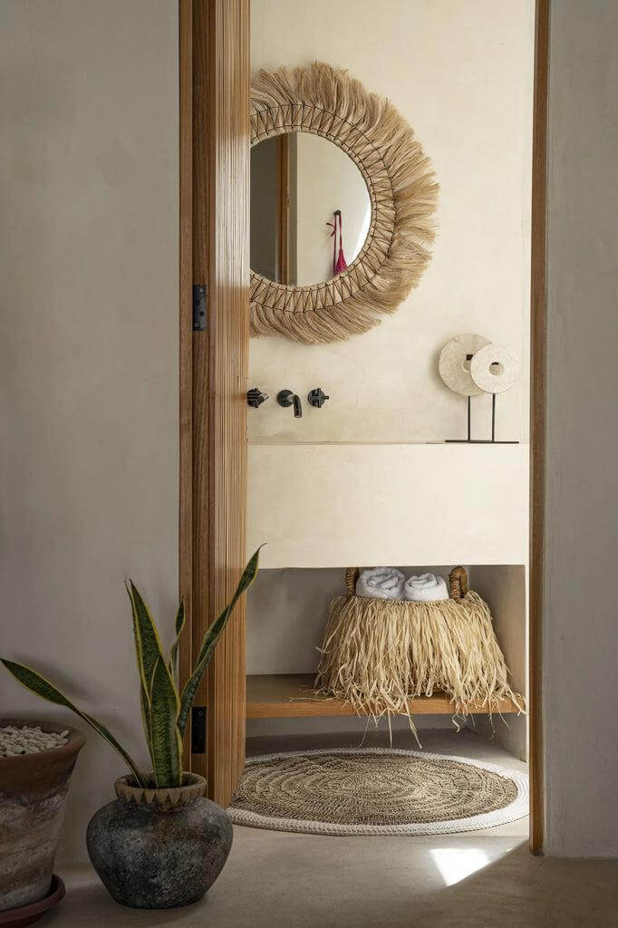 Stijlvolle badkamer met spiegel omlijst in tropische raffia, natuurlijke decor en potplant, ideaal voor een ontspannen sfeer.