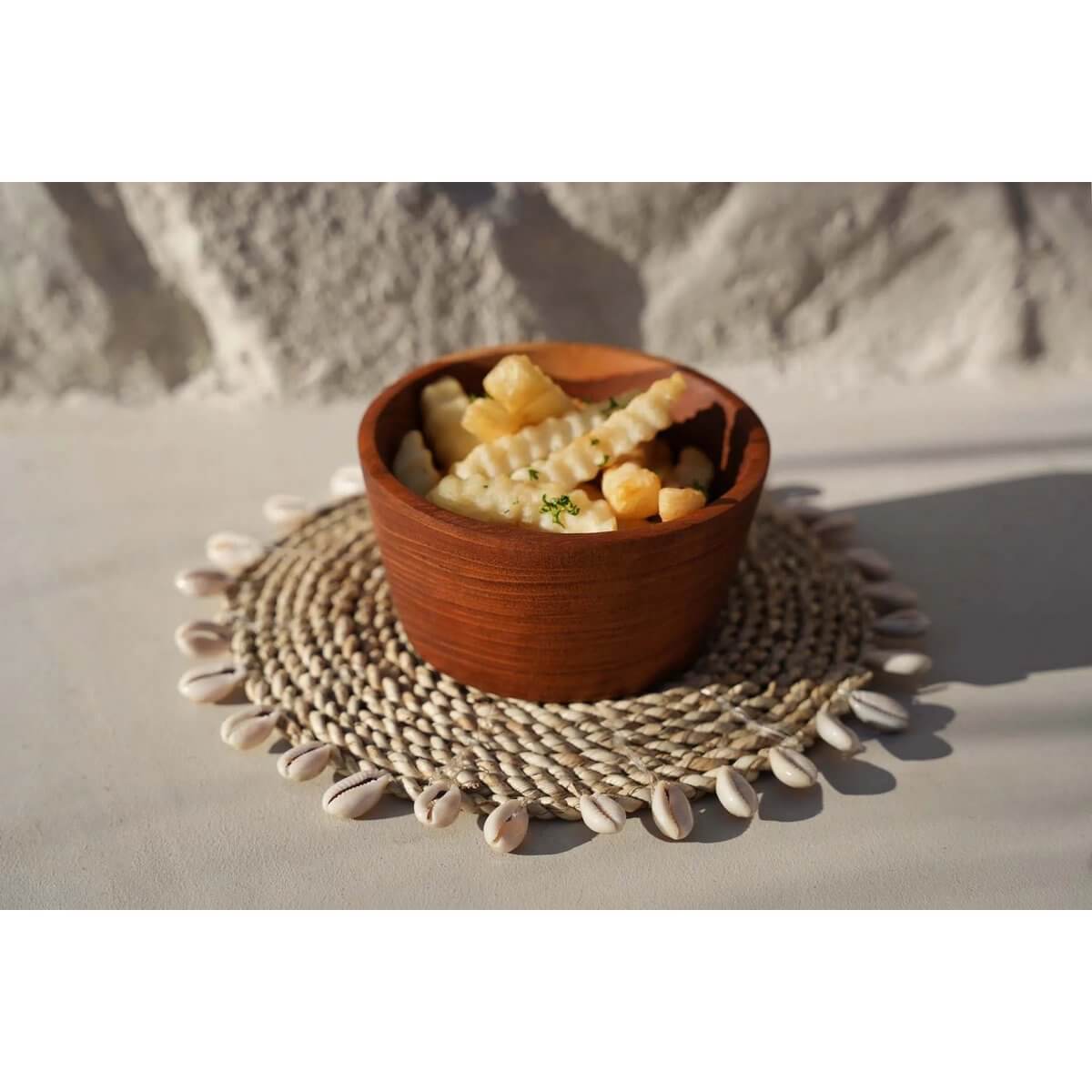 Bohemian-style raffia and shell trivet with wooden bowl, perfect for adding island charm to any table setting.