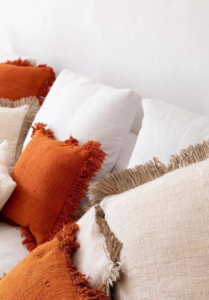 Kussenhoes De Saint Tropez in naturel wit en oranje met raffia franjes op een bank, boho stijl, formaat 60x60 cm.