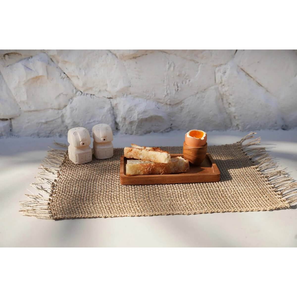 Salt & Pepper Sumba shakers made of sandstone, shaped like stone men, on a Bohemian-style mat next to a wooden tray.