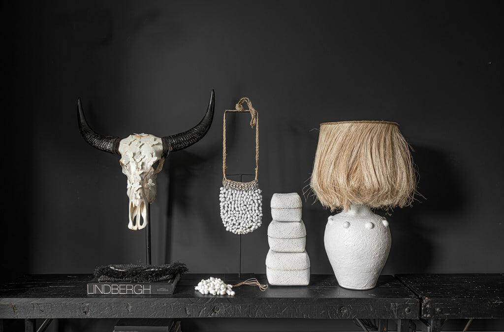 Boho chic interieur met handgemaakte Shell Purse uit Indonesië, schedel en keramische kunststukken op zwarte achtergrond.