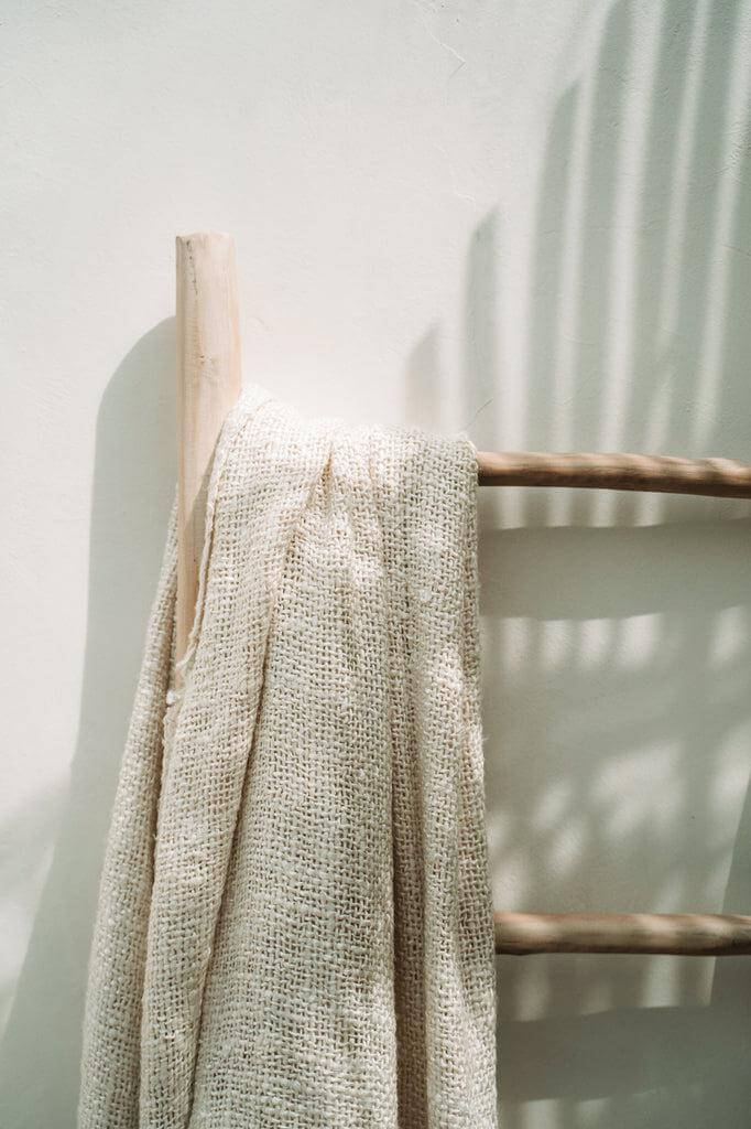 Luxe handgeweven katoenen plaid in crème op houten ladder, met zijden uitstraling en franjes, wafelstructuur, gezellige thuisdecoratie.