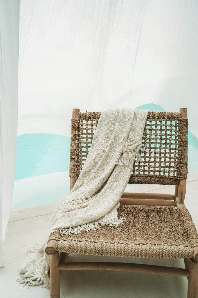 Luxe handgeweven crème plaid met franjes op rotan stoel, perfect voor een warme, gezellige sfeer in uw interieur.