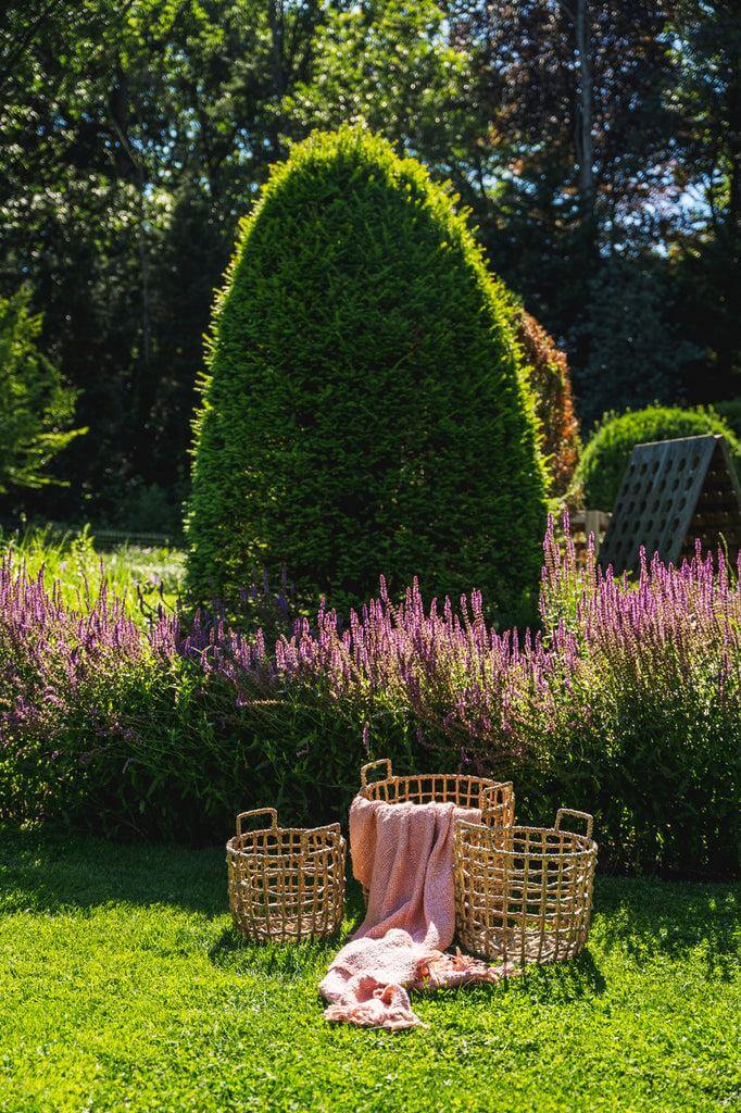 Salmon pink plaid draped over woven baskets in a sunny garden.