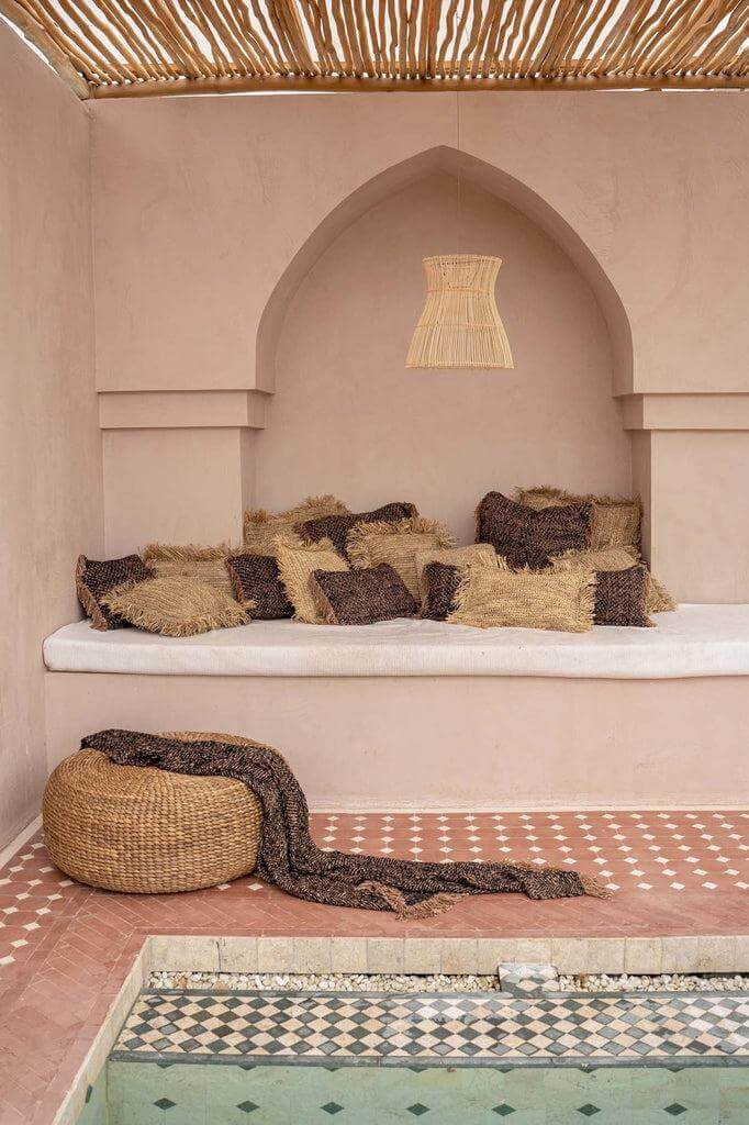 Gezellige zithoek met kussens en plaid bij zwembad, perfect voor een warme, stijlvolle sfeer.