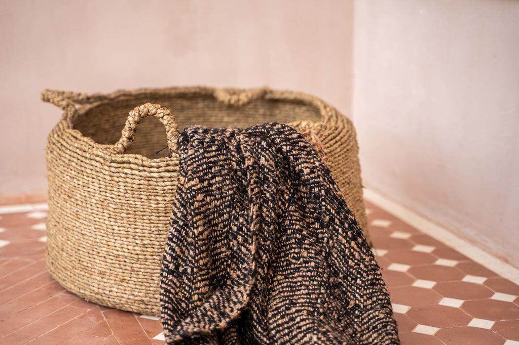 Zwart Koper plaid met wafelstructuur en franjes over een rustieke mand, perfect voor een warme, gezellige sfeer in huis.