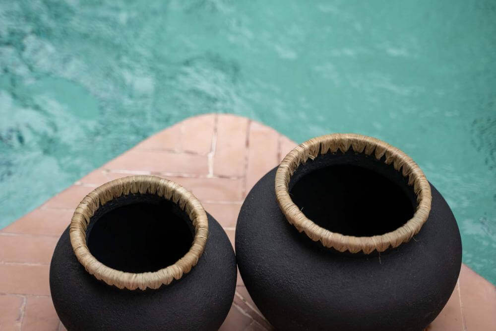 Twee zwarte terracotta vazen met raffia details aan de rand, geplaatst bij een zwembad. Perfect voor droge bloemen.