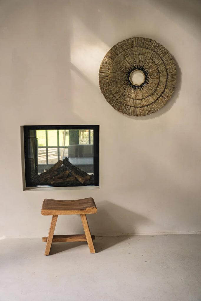 Suar kruk in natuurlijke stijl naast een moderne haard en wanddecoratie, perfect voor eetkamer, slaapkamer of terras.