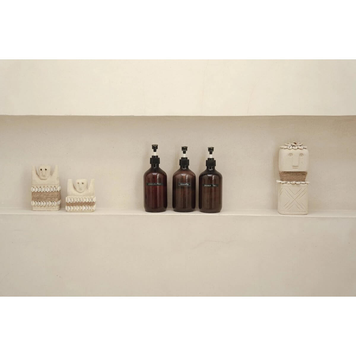Bohemian decor: Hand-carved Sumba stone statues and modern brown bottles on a minimalist shelf. Perfect for unique home styling.