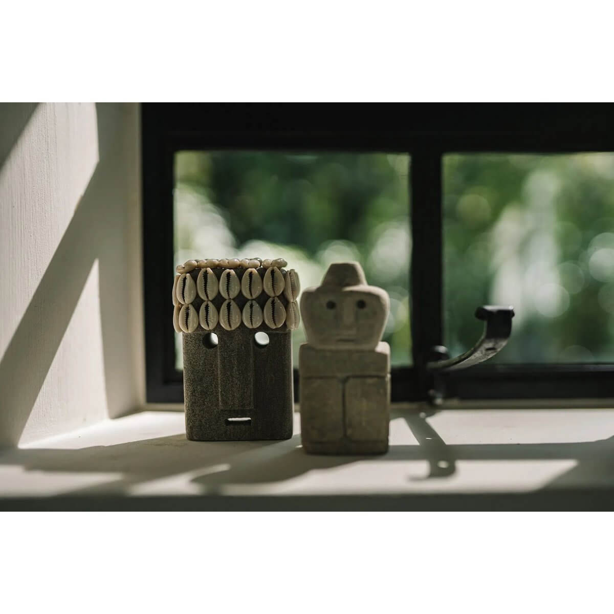 Bohemian Sumba stone figures, hand-carved from sandstone, displayed by a window, capturing traditional Indonesian craftsmanship.
