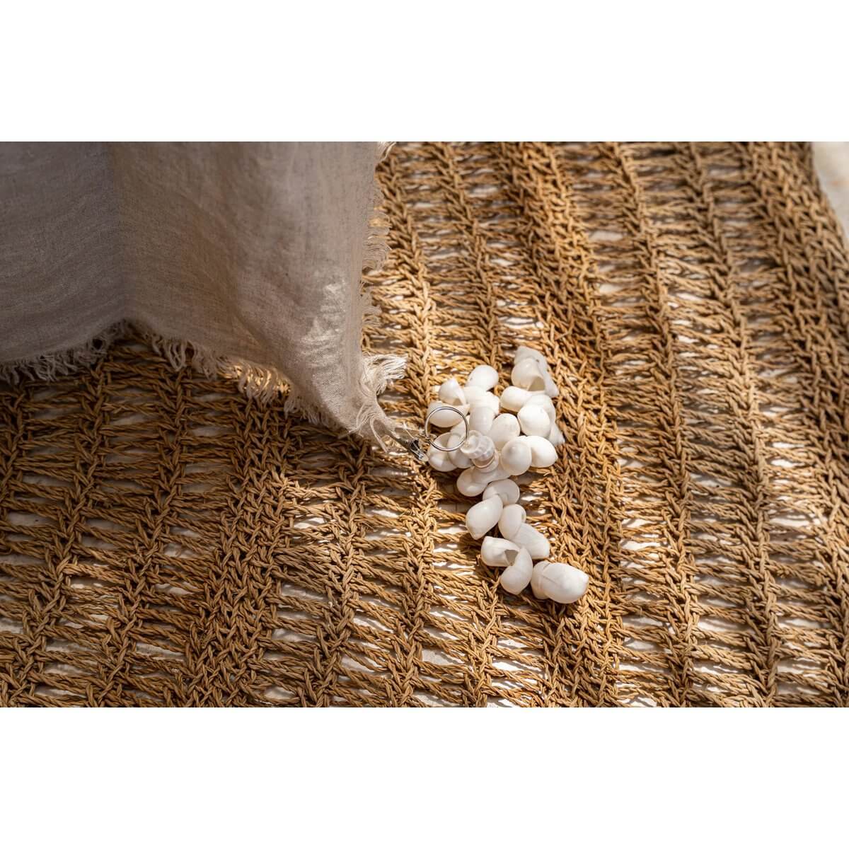 Close-up of a bohemian coastal-style white tafelkleedhanger with shells, on a woven mat, enhancing outdoor dining decor.