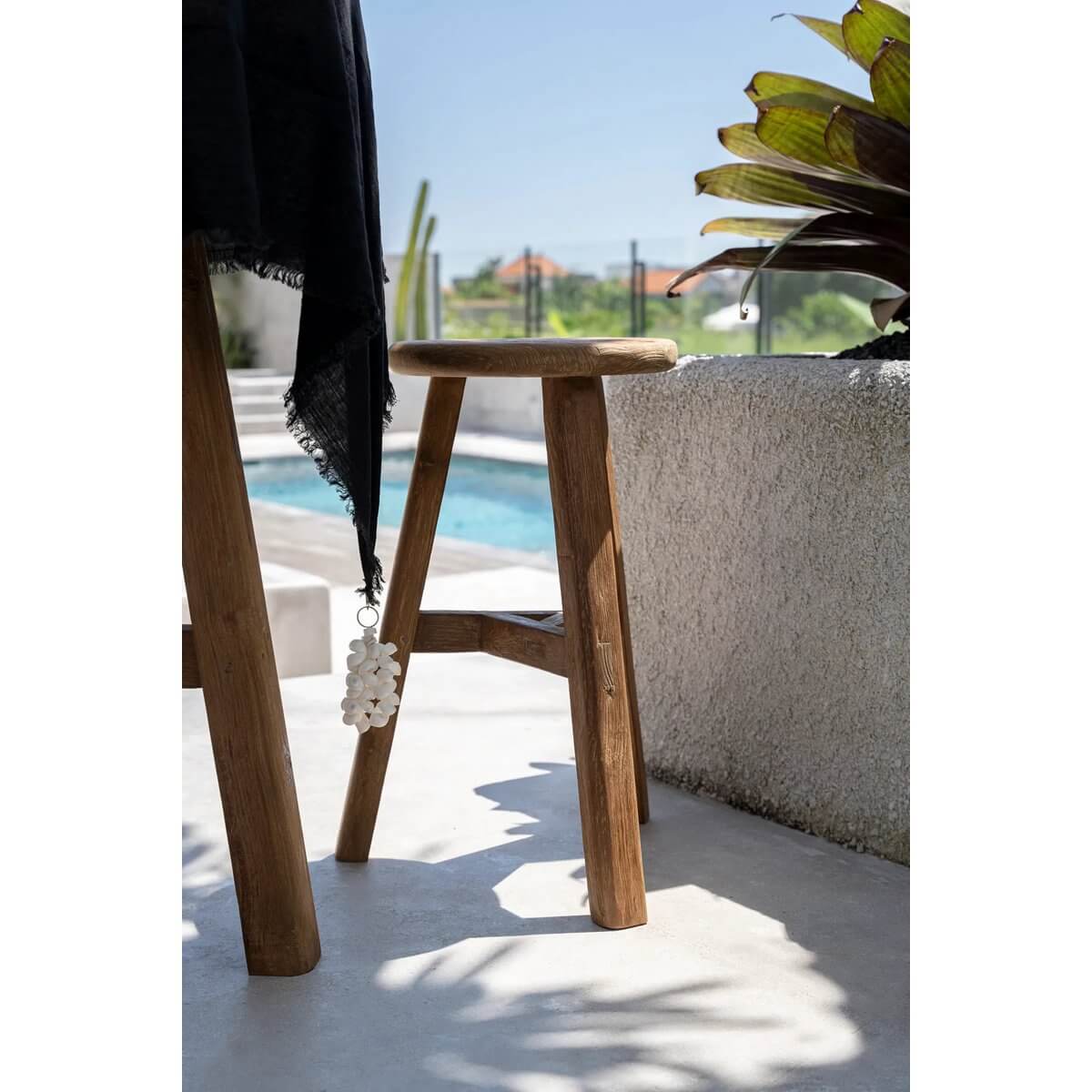Bohemian style table with white tablecloth hanger by the pool, featuring seashell accents and wooden furniture for an elegant coastal look.