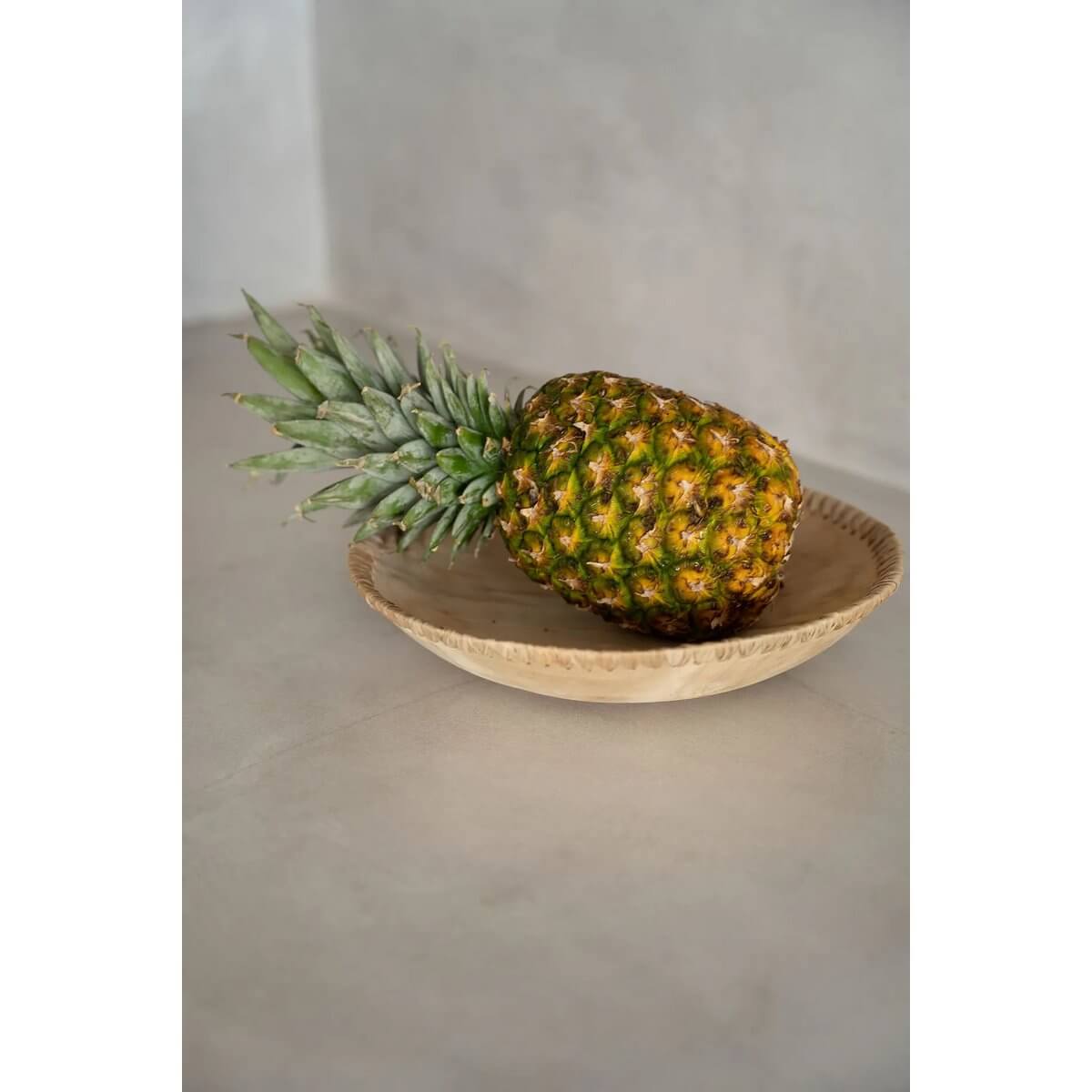 Ananas geplaatst in een elegante, natuurlijke teakhouten kom, perfect om uw tafel een rustieke uitstraling te geven.