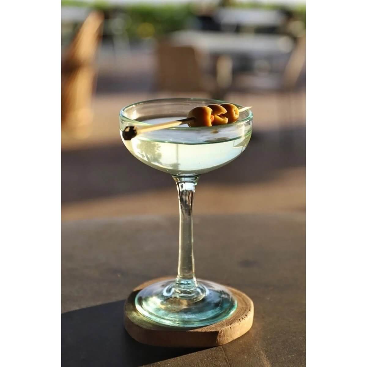 Martini glass on a teak root boho coaster with olives, perfect for a chic summer table setting. Versatile, natural bohemian style.