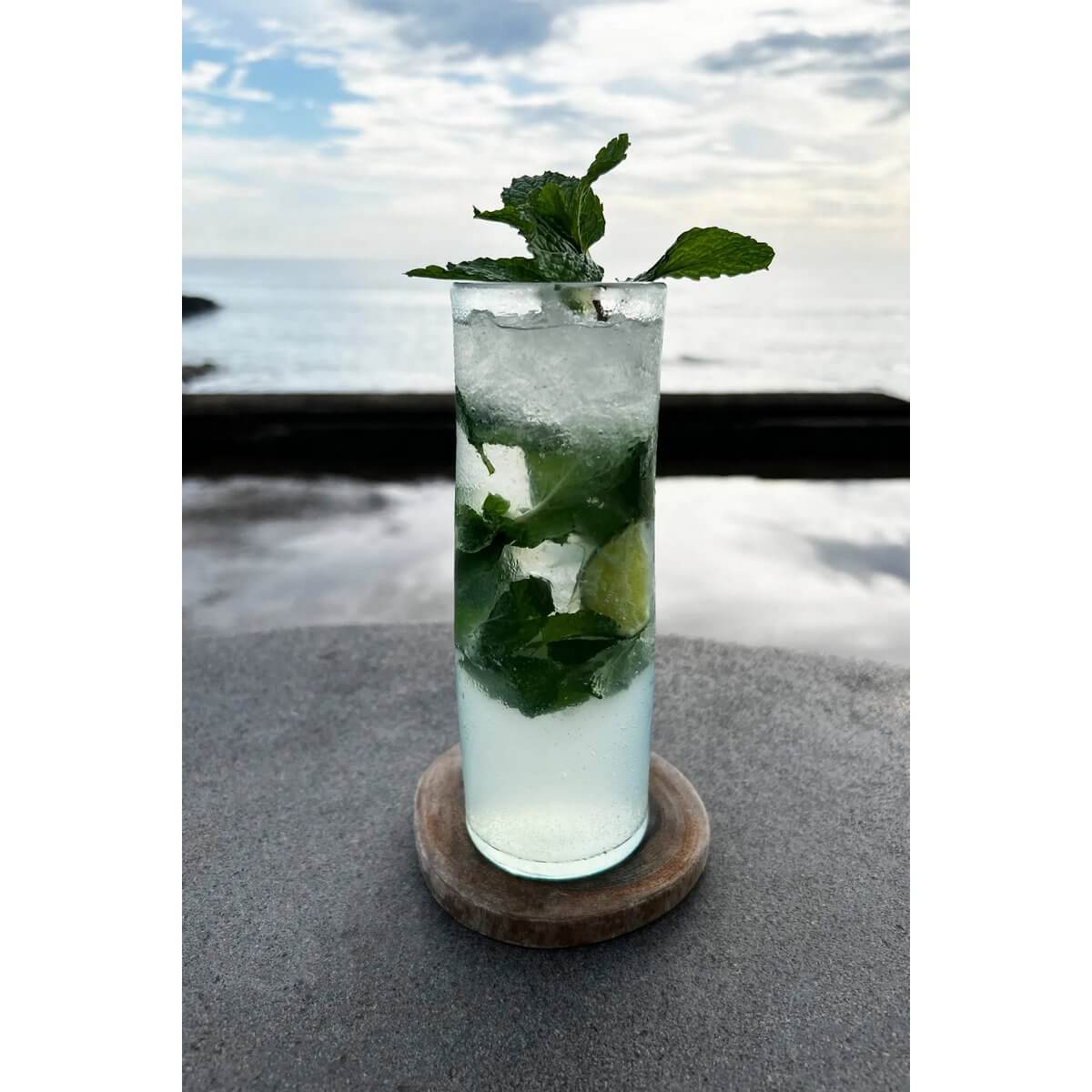 Bohemian teak root coaster holding a refreshing mint cocktail by the sea, enhancing any boho-chic summer table setting.