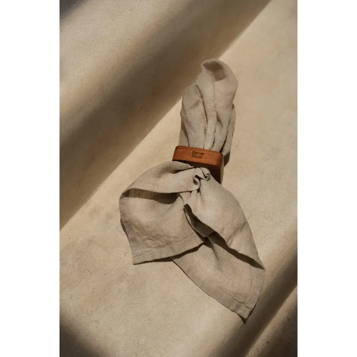 Bohemian style teak root napkin ring set on folded linen against a soft beige background, showcasing rustic elegance.