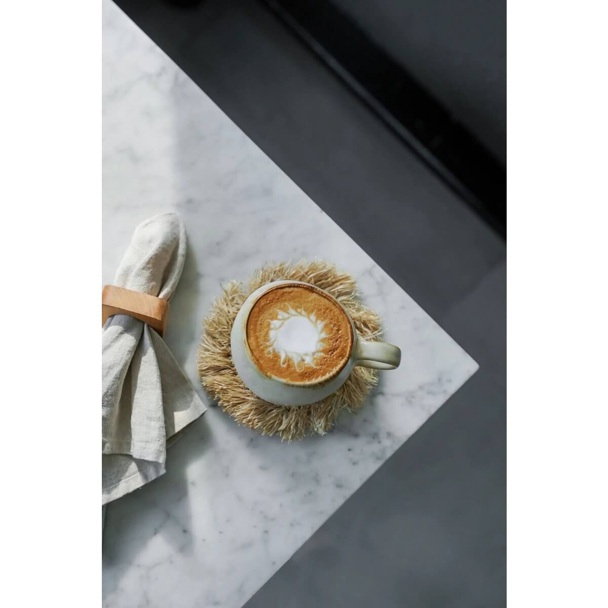 Bohemian-style coffee scene with latte in ceramic mug and rustic cloth napkin on marble table.