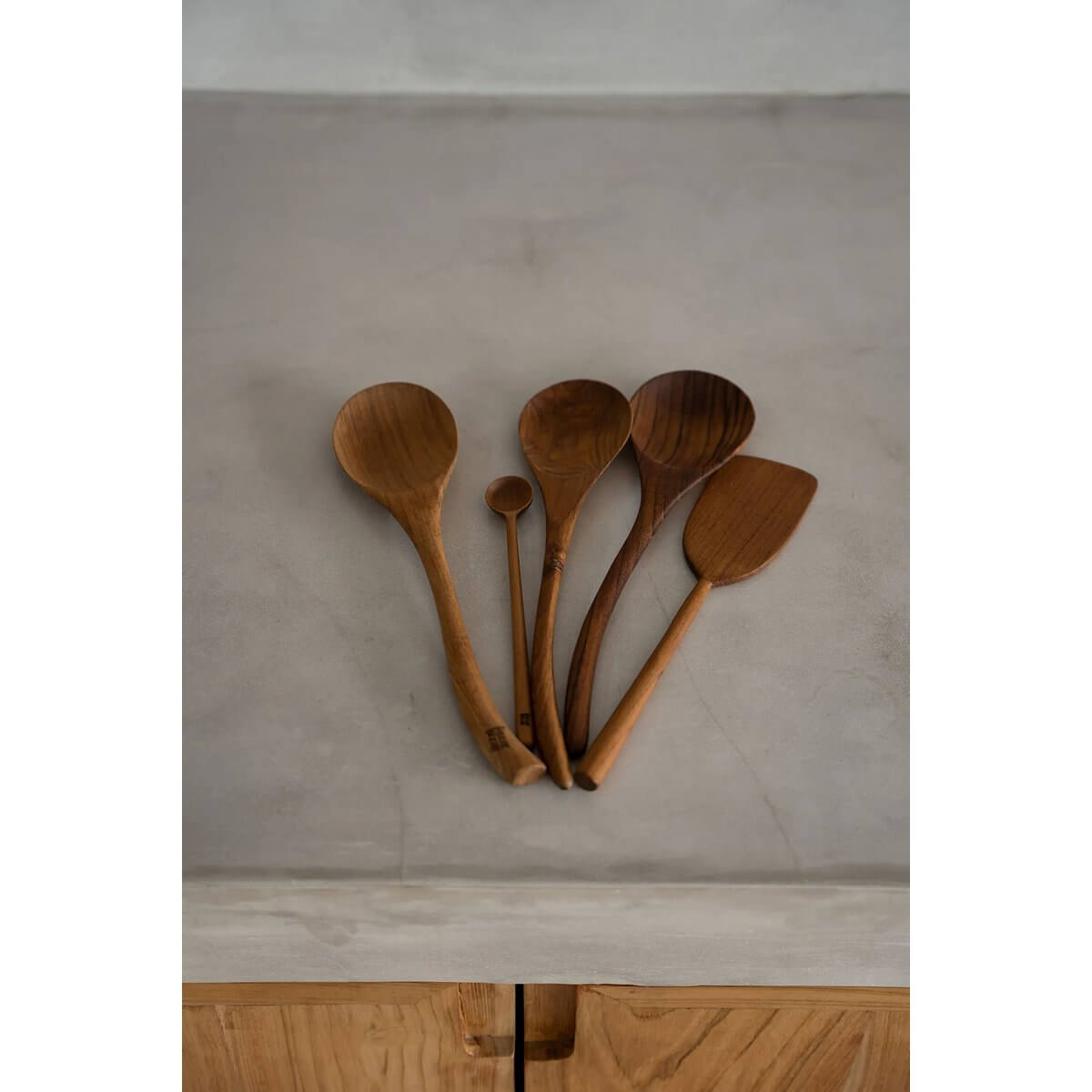 Set of handcrafted bohemian-style teakwood spoons on a gray surface, perfect for stylish dining settings. Made by Bazar Bizar Living.