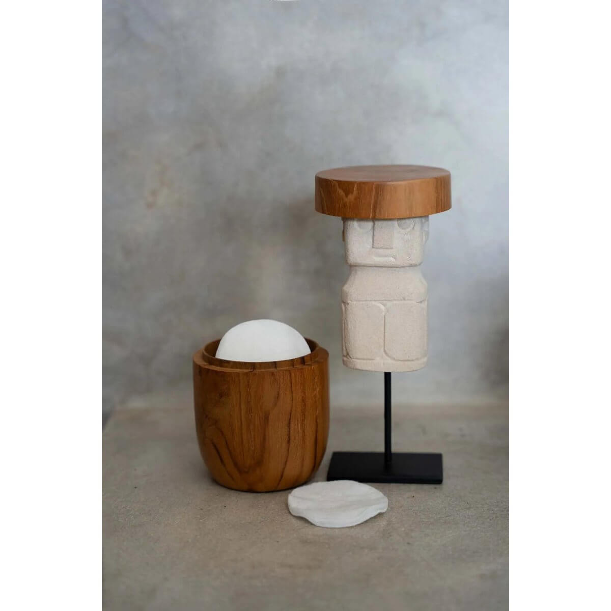Sculptural Bohemian decor with teak bowl and carved stone figure on stand, blending natural elegance and artistic design.