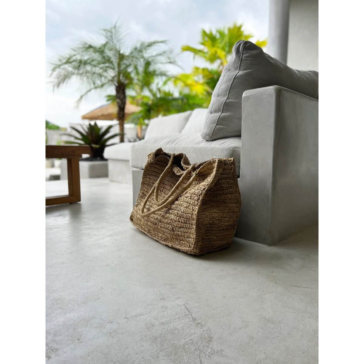Raffia De Ti Amo-shopper naast een stijlvolle, moderne sofa, ideaal voor een dagje strand of winkelen. Ruim en licht ontwerp.