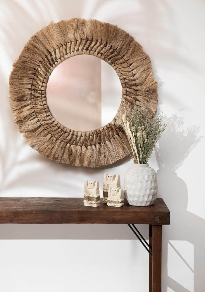 Rustieke woonkamerinrichting met rieten spiegel, houten tafel en decoratieve vaas met gedroogde bloemen.