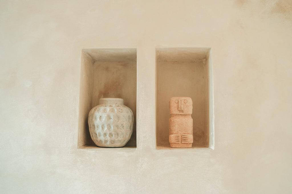 Terracotta vaas en beeld in nissen tegen een beige muur voor een moderne en minimalistische uitstraling.
