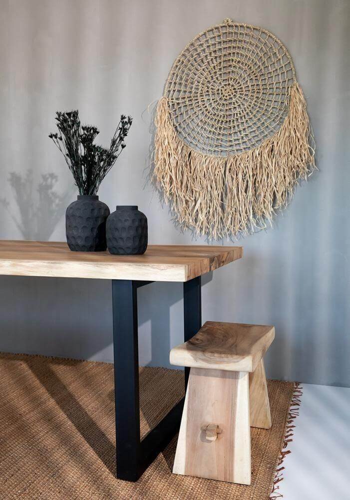Zwarte terracotta vaas op houten tafel met gedroogde bloemen naast macramé decor tegen grijze muur.