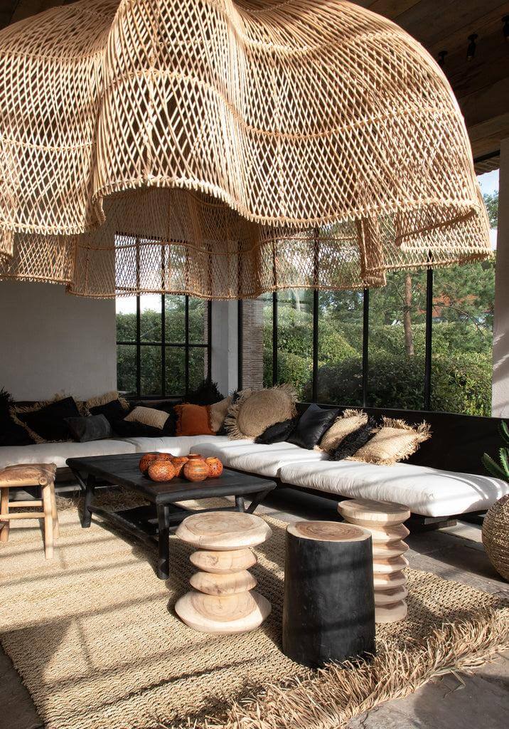 Stijlvolle woonkamer met De Tribe Kruk in zwart, natuurlijke tinten en een organisch ontwerp met rieten lamp. Perfect voor elk interieur.