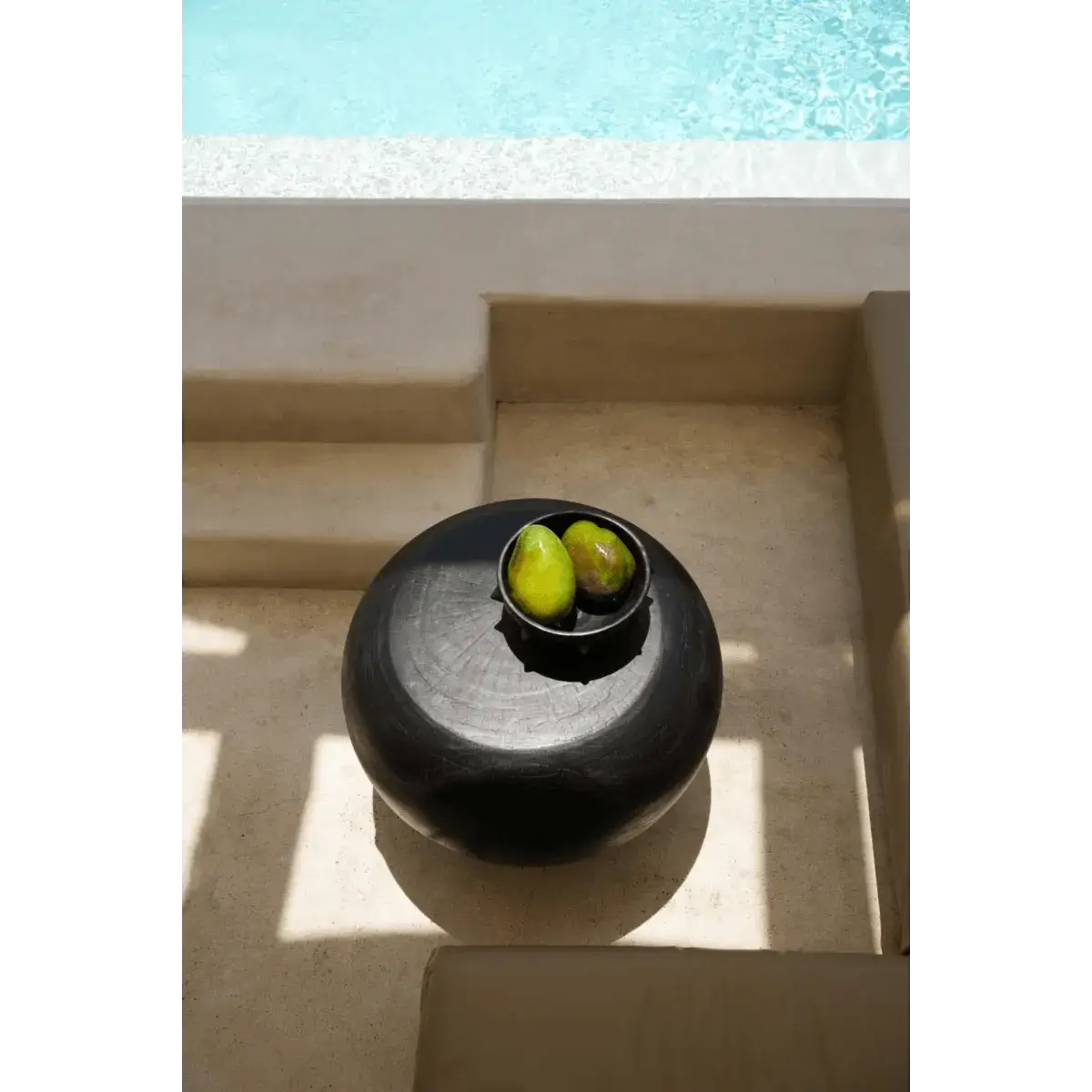 De Tutup Salontafel in zwart suarhout, geïnspireerd door de vorm van een kwal, met een bohemian uitstraling naast een zonnig zwembad.