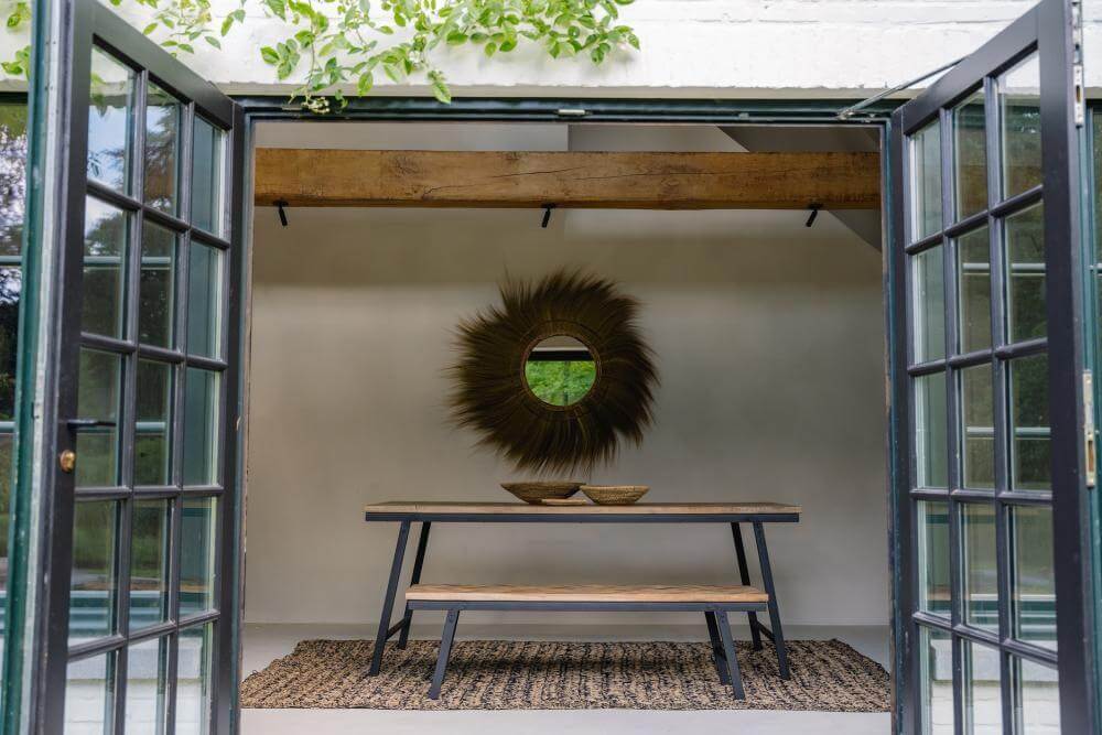 Stijlvolle teakhouten visgraatbank met zwart ijzeren frame in gezellige binnenruimte met natuurlijke decoratie.