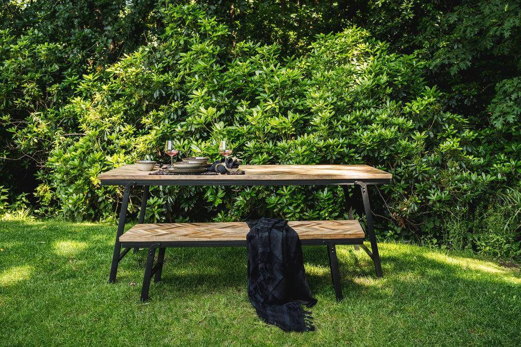 Teakhouten visgraat bank en tafel op grasveld in een tuin, ideaal voor binnen en buiten gebruik, met zwart ijzeren details.