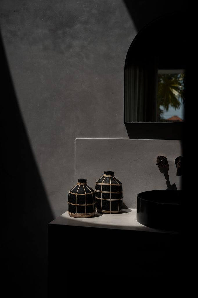 Zwarte De Whoopy vaas met rotan detail in een sfeervolle ruimte, perfect voor droogbloemen. Stijlvolle terracotta decoratie.