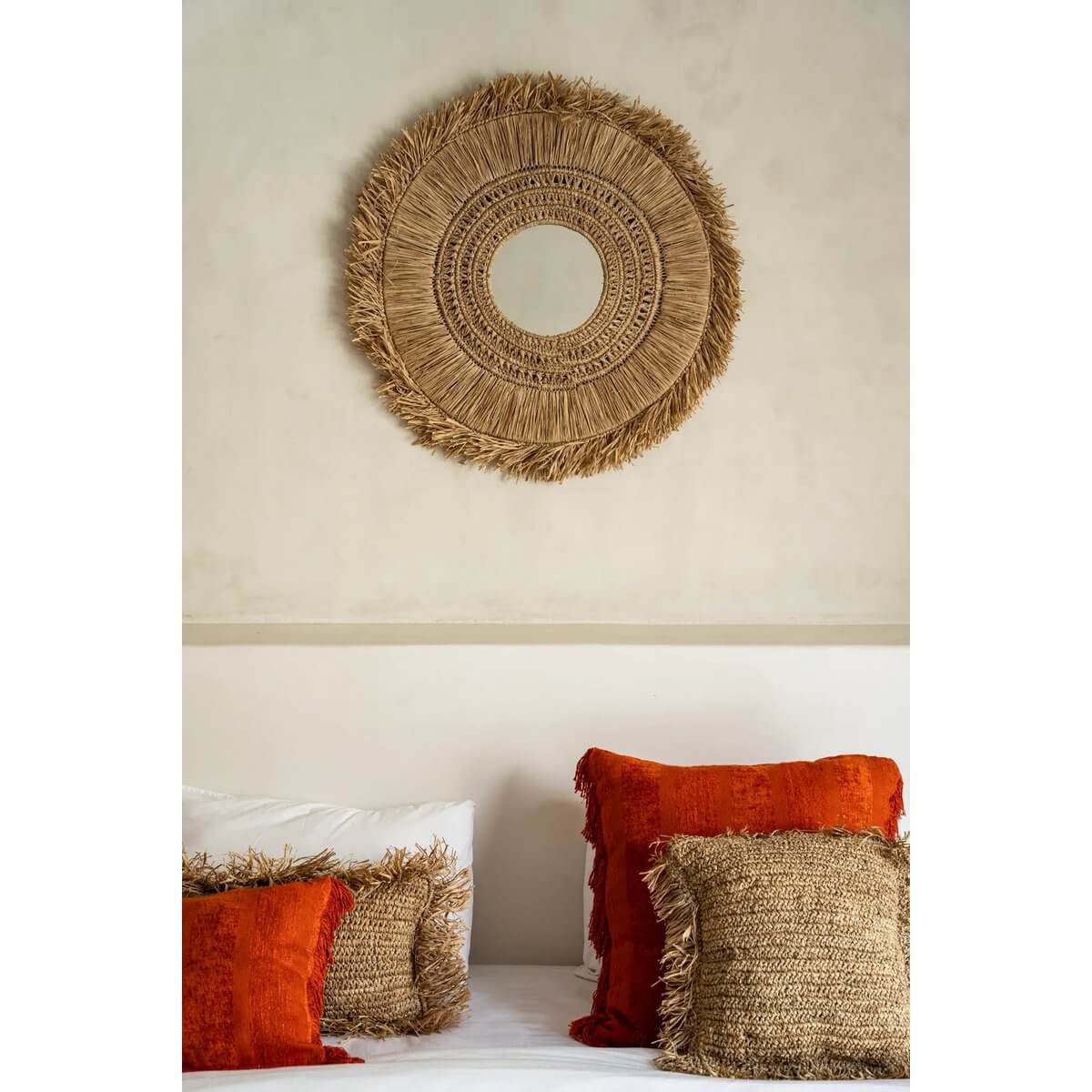 De Yuki-spiegel van raffia boven een bed met oranje kussens, straalt kustsfeer uit in natuurlijke kleuren.