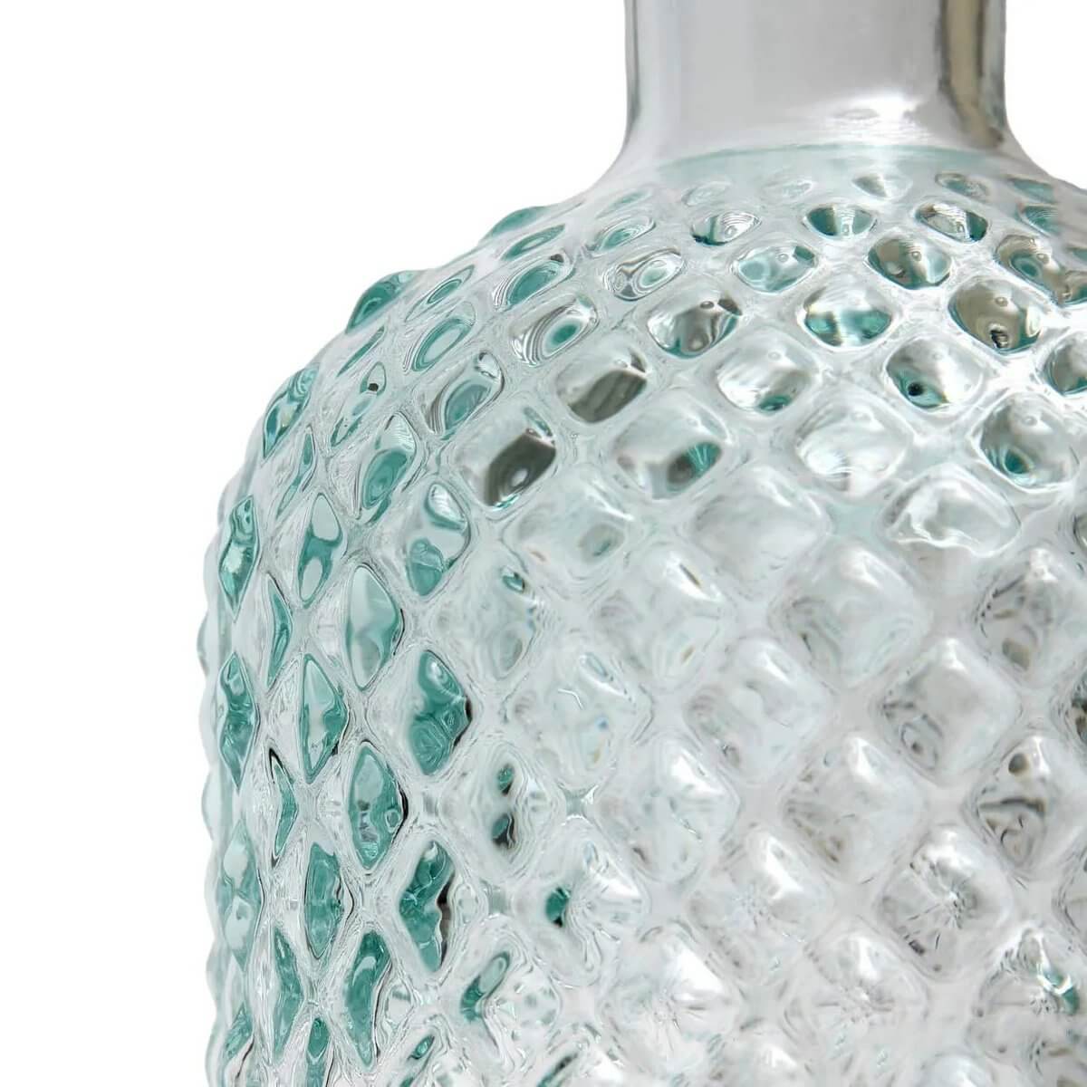 Close-up of a textured, clear glass bottle with elegant, diamond-like patterns, perfect for a bohemian and refined lifestyle.