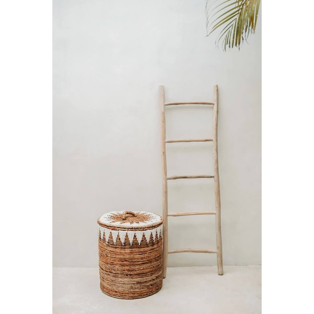 Handgeweven bananenblad wasmand met wit grafisch patroon naast houten ladder voor bohemian interieurstijl.