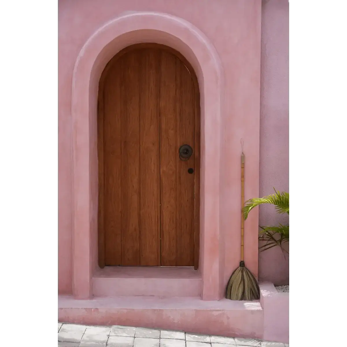 Bohemian Indonesian broom made of grass beside a rustic pink arched door, perfect for interior decor by Bazar Bizar Living.